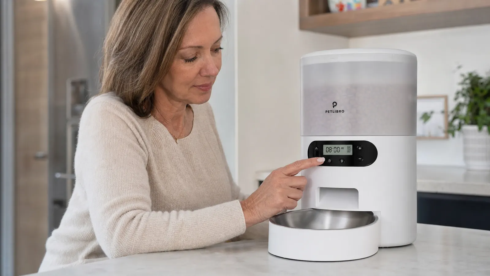 Hands connecting a PETLIBRO automatic feeder power cord and opening the top hopper lid to fill with dry kibble